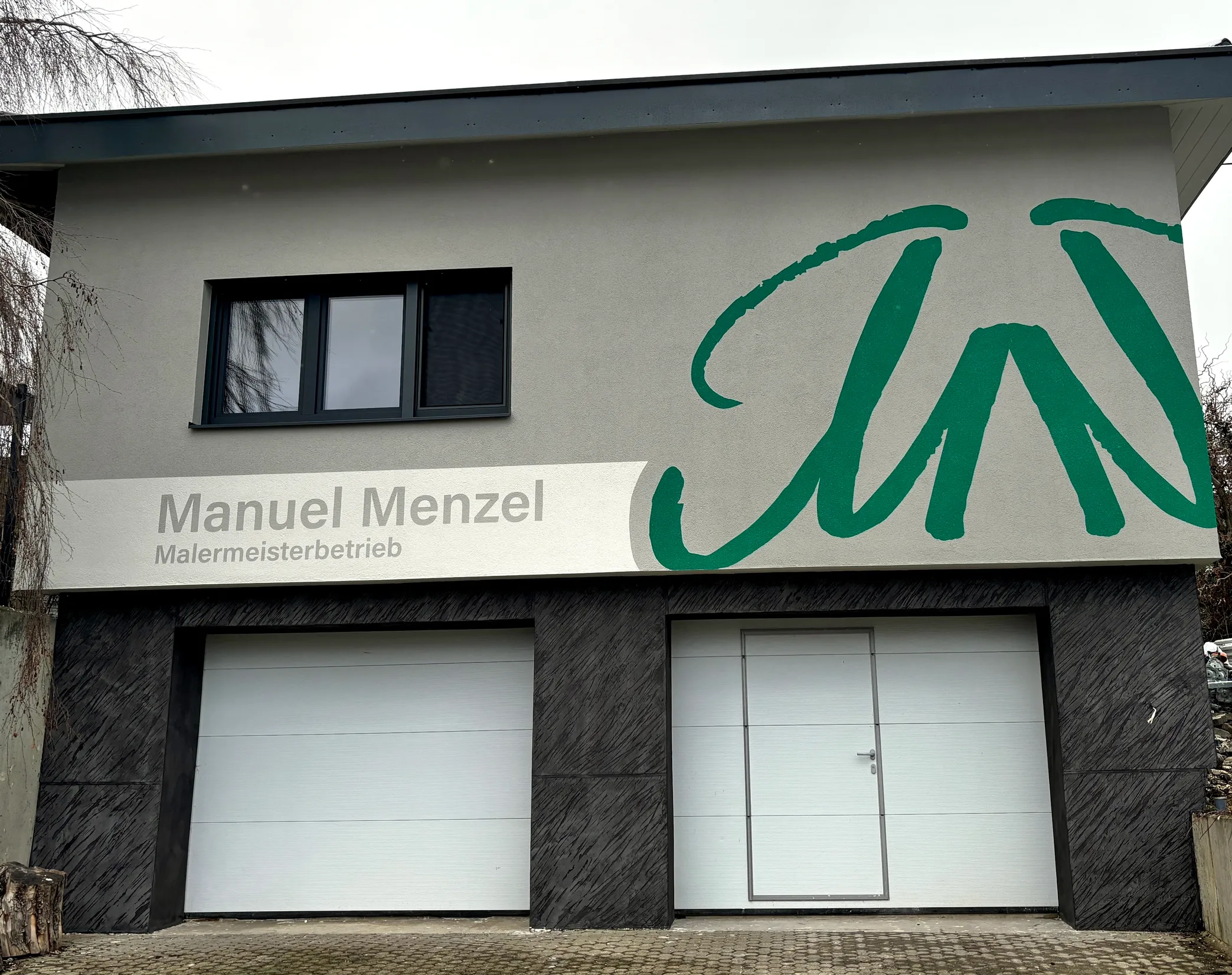 Firmengebäude von Malermeister Menzel in Durchhausen mit dem Schriftzug „Manuel Menzel Malermeisterbetrieb“ und dem grünen Logo an der Fassade